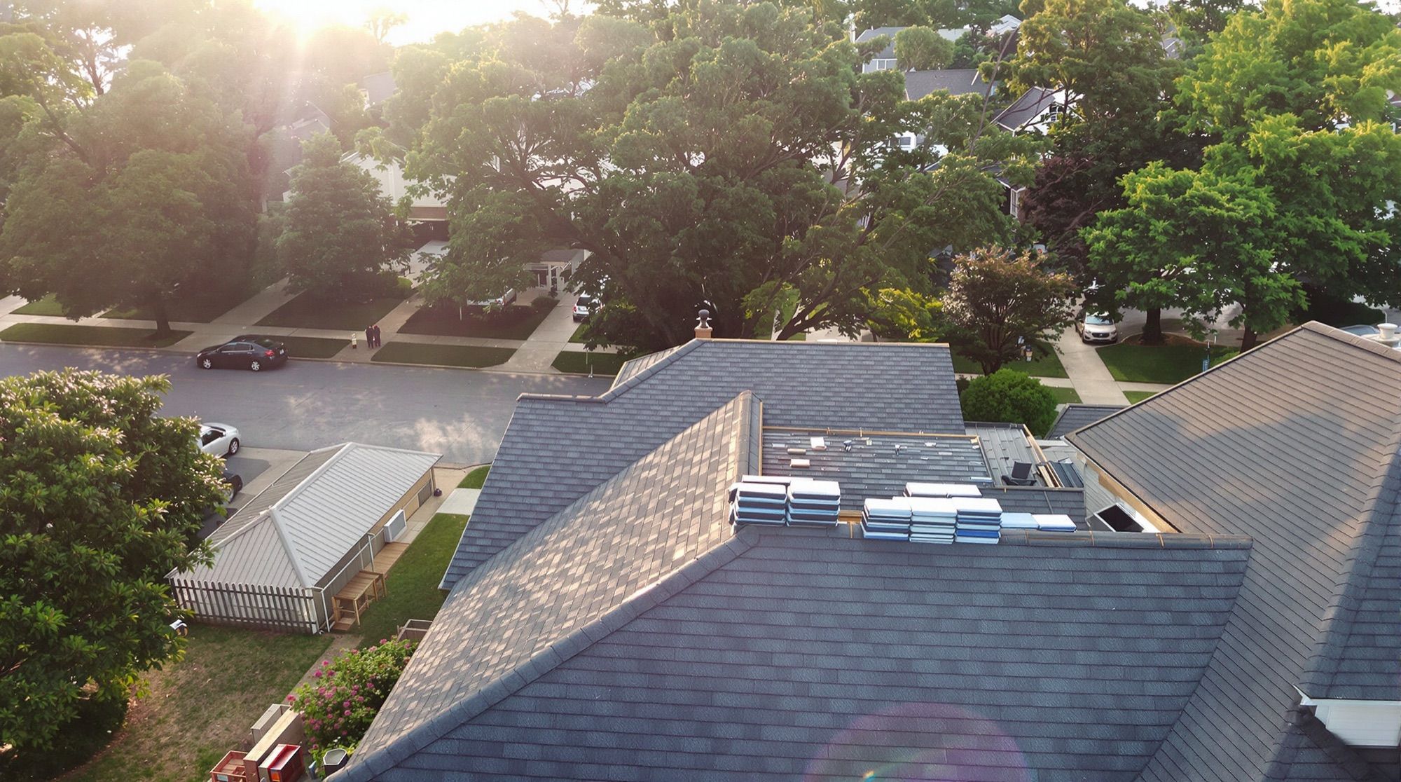 Suburban street of shingle roofs from above, one roof mid-replacement with bundles on the ridge