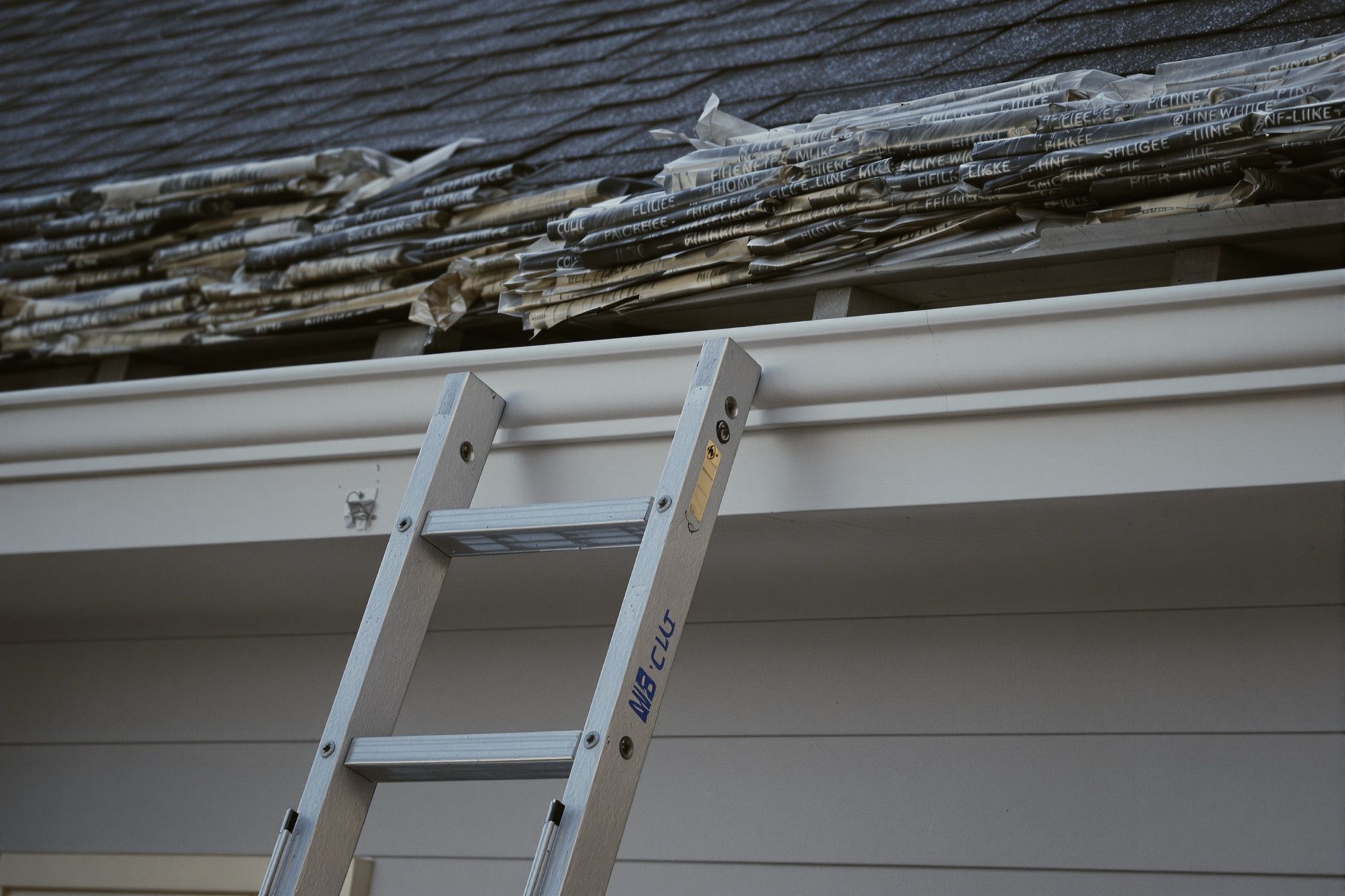 Ladder against a gutter at dawn with shingle bundles on the roof edge
